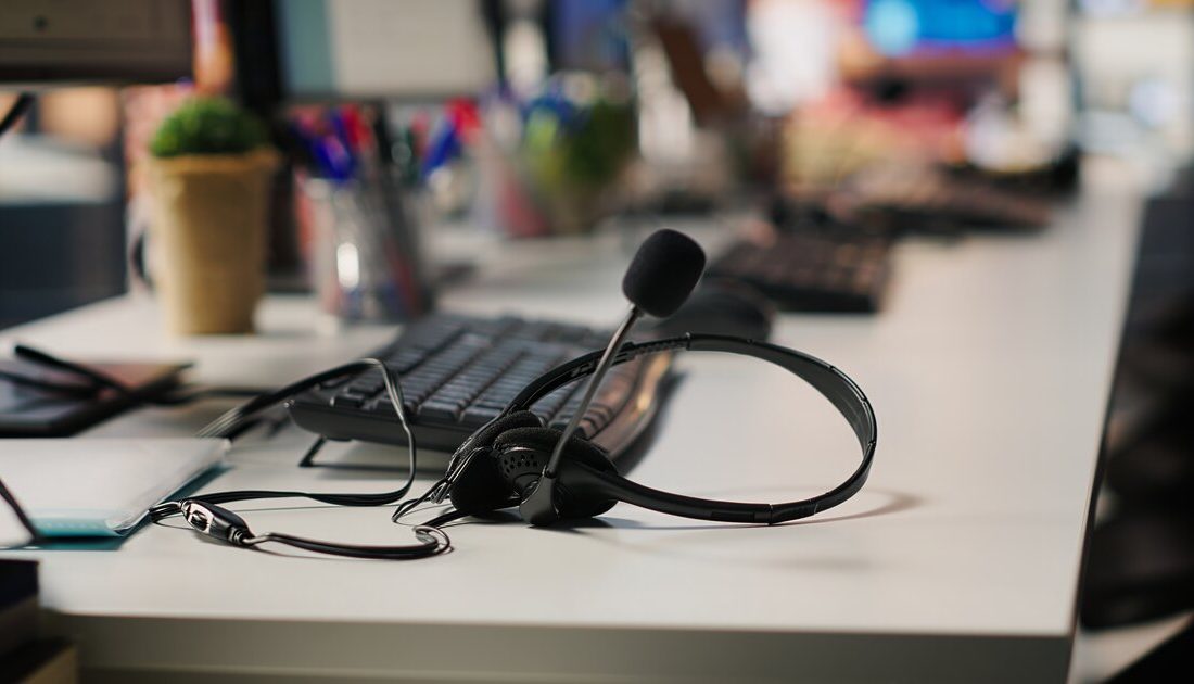 Contact-centre headset with microphone resting on a customer-service workstation desk