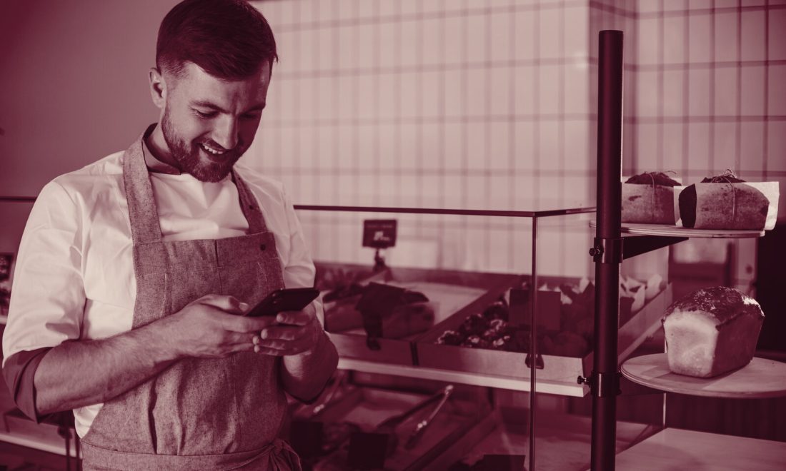 Bakery owner checking his phone at the counter, wine-toned local business analytics concept