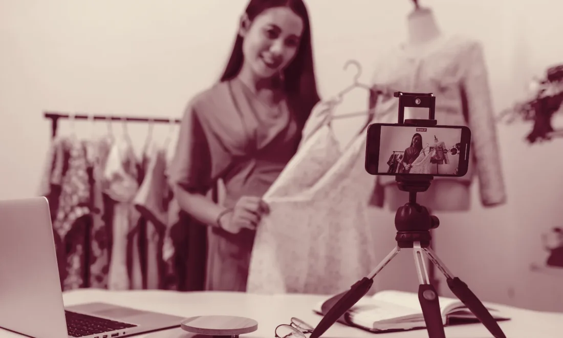 A seller live-streams clothing to a smartphone on a tripod, illustrating Meta live video shopping ads