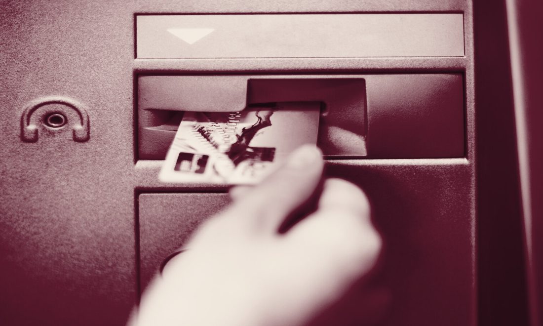 A bank card being inserted into a card slot, shot in a deep wine tone