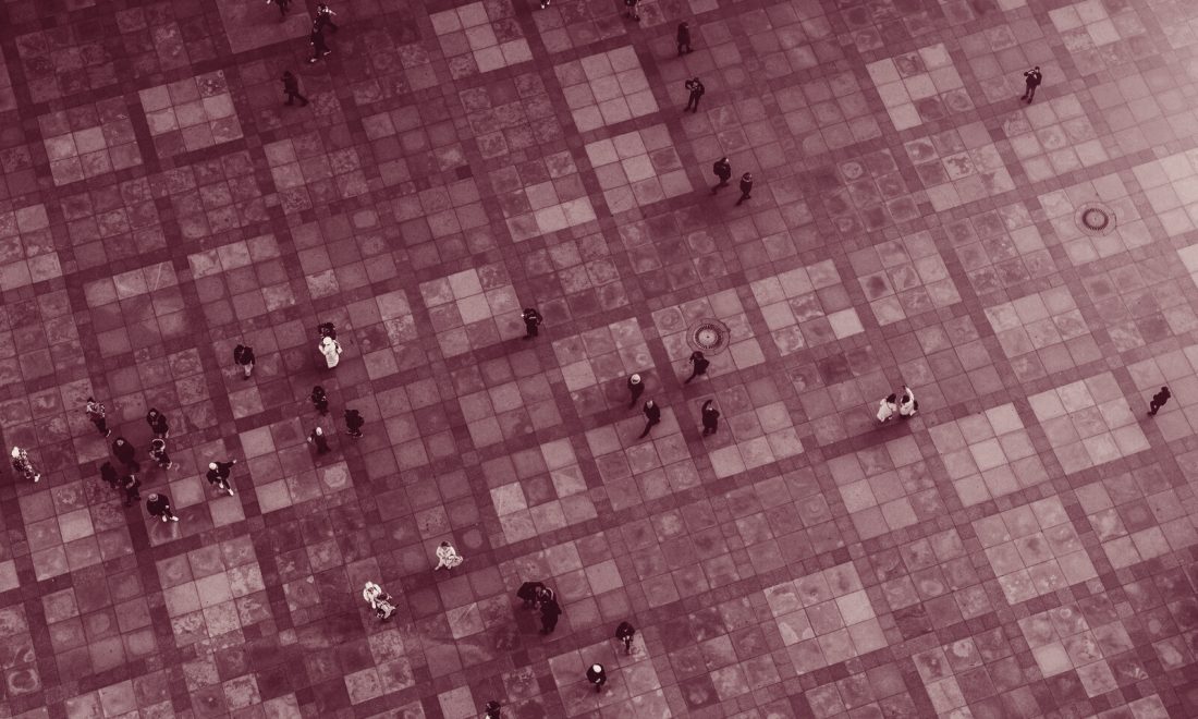 Aerial view in wine tones of scattered individual people walking across a large grid of paving slabs