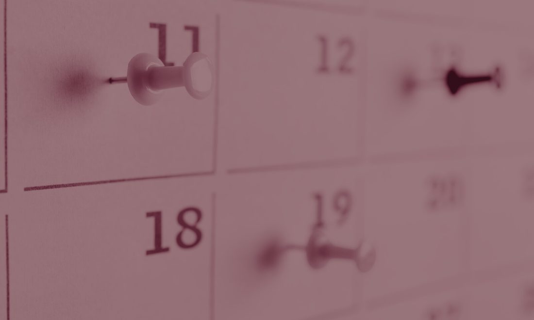 Close-up of a wall calendar with push pins marking days, wine-toned