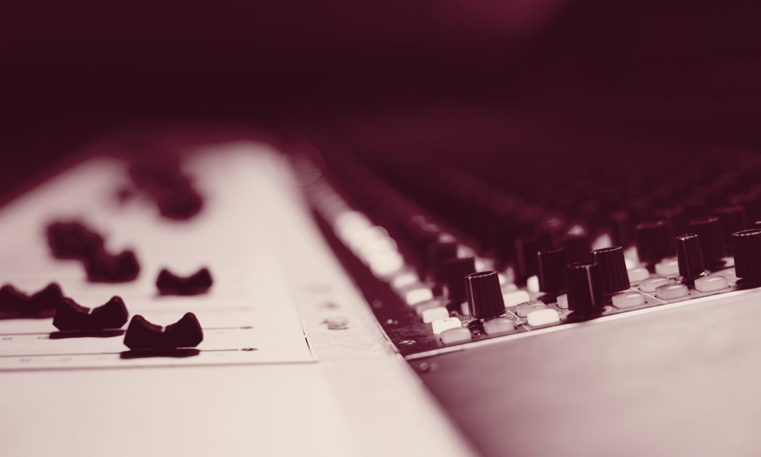 Wine-toned close-up of a mixing console with faders and rows of knobs