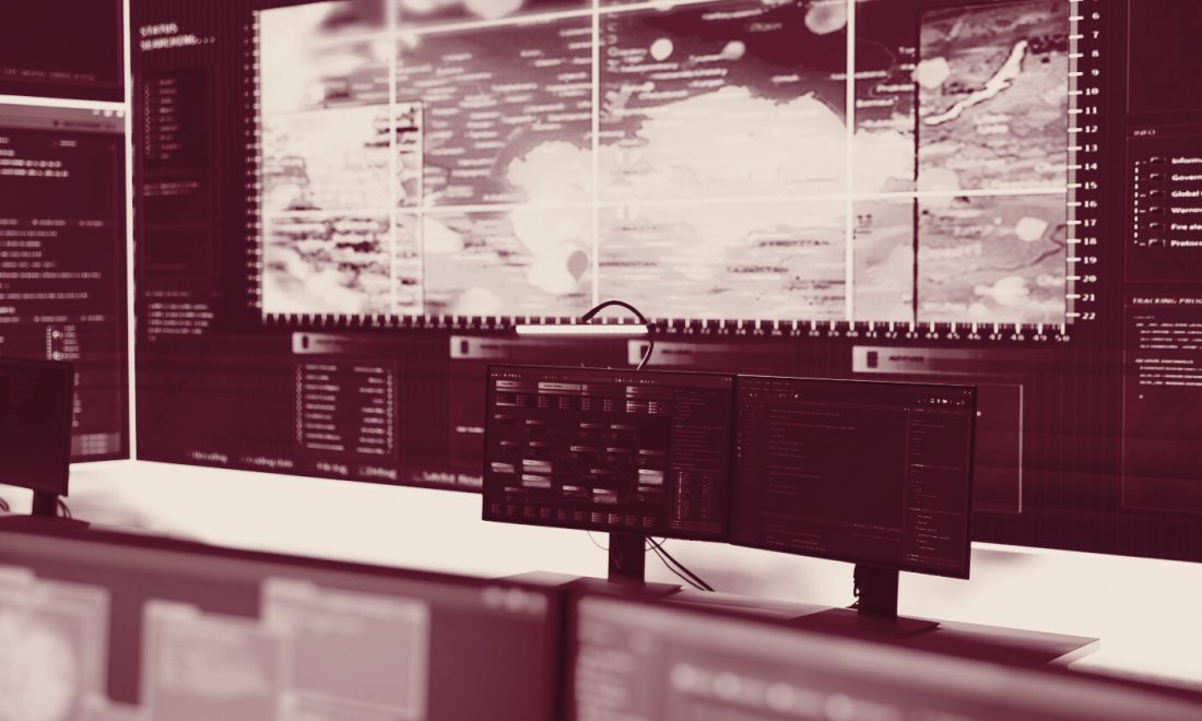 A large status wall of monitoring screens above empty desks in a darkened operations room