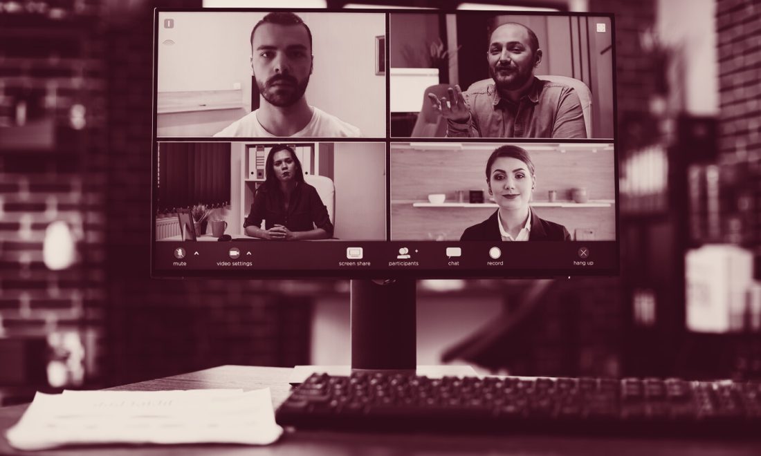 Four participants in a video meeting on a monitor, with a record button visible in the call toolbar