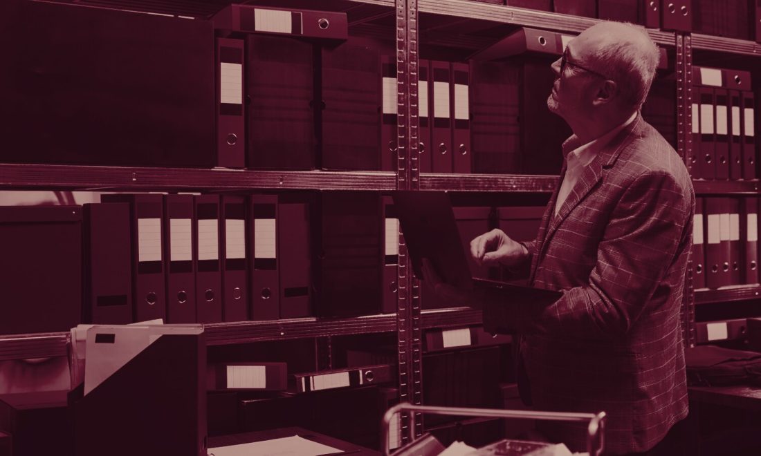 An investigator searching shelves of bound files in an archive room, in wine tones