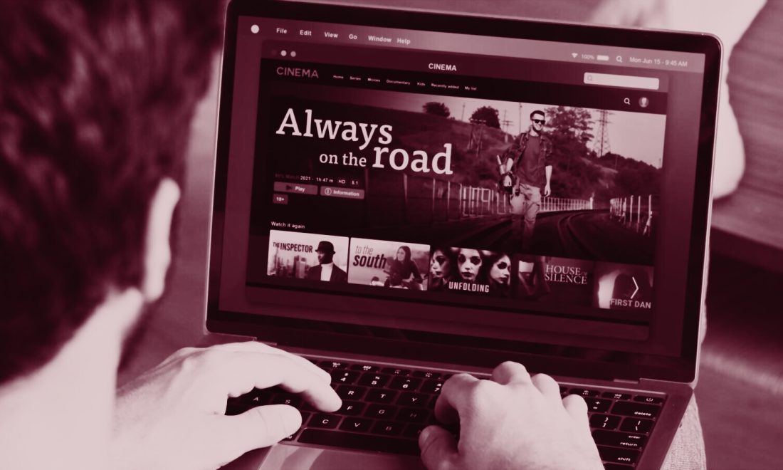 Hands on a laptop keyboard with a streaming catalogue open and a play button on the screen