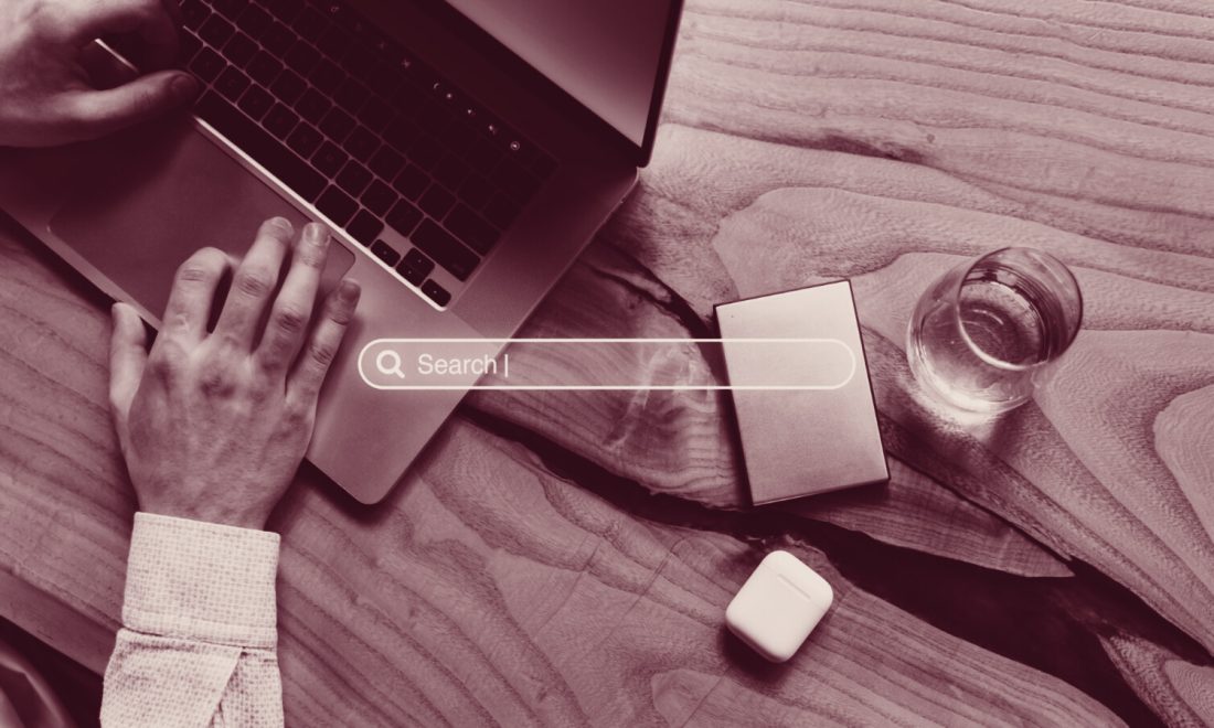 Hands on a laptop beside a search bar overlay, in wine tones