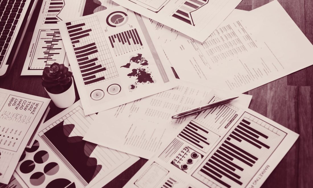 Printed analytics reports with bar charts and pie charts spread across a desk, wine-toned