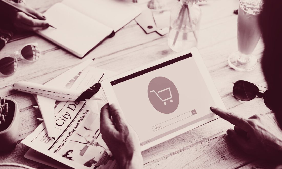 Hands holding a tablet with an online shop cart page beside a lifestyle magazine on a table, wine-toned photo