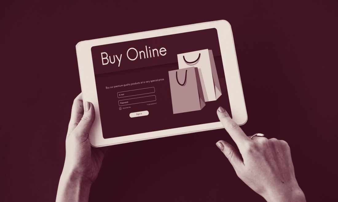 Hands holding a tablet with a Buy Online sign-in form and shopping bags, in a wine tritone