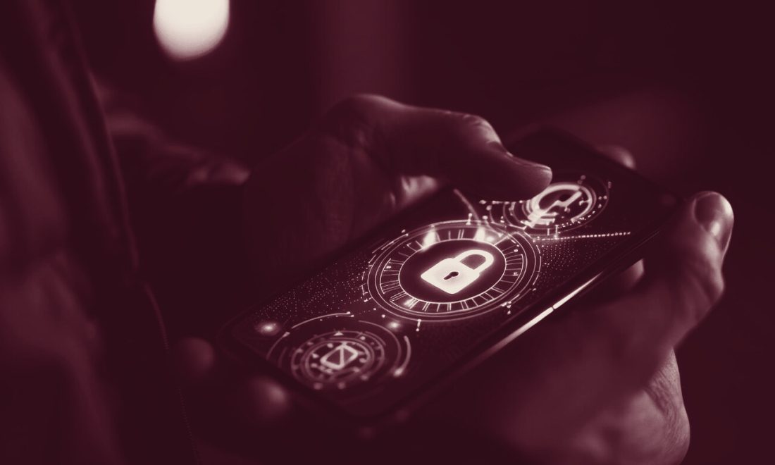Hand holding a smartphone with a padlock icon on screen, in wine tones, illustrating the Safari iOS 27 block on ad domains